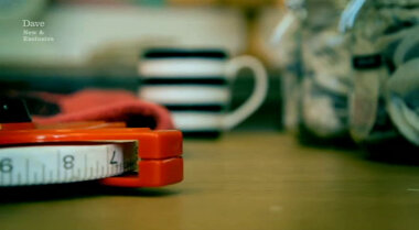 Shallow focus image of a tape measure, a ceramic mug, a tea towel, and some jars of teabags.