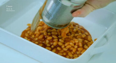 Image of a tin of baked beans being poured into a ceramic baking dish.