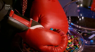 Image showing one of the contestants (specifically, Frank Skinner) separating an individual blue sweet while wearing boxing gloves.