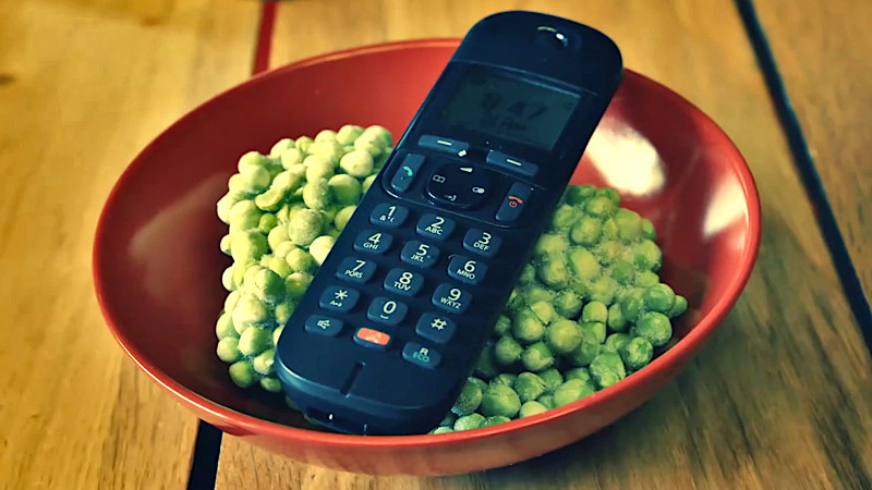 A 2000s-style cordless home phone handset lying on top of a bowl of frozen peas.