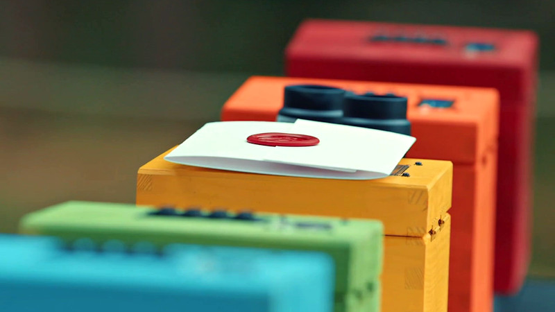 Five colourful wooden boxes in a row, with the task envelope on top of one, and binoculars laid inbetween them.