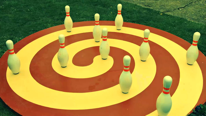 Bowling pins set up evenly on top of a round wooden board with a red and yellow swirl painted on it.