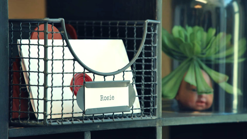 An envelope in a wire container labelled 'Rosie' on a shelf.