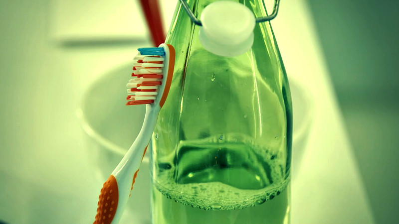 A toothbrush rests on a green glass bottle.