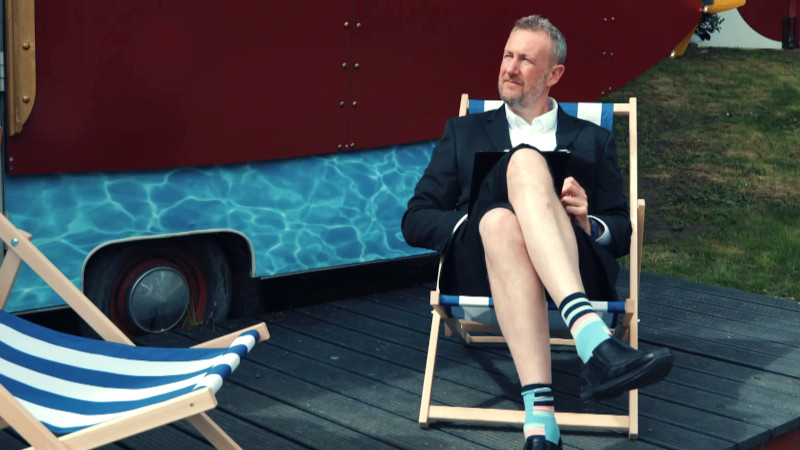 Alex Horne in a beach chair with his pale calves exposed to the viewer.