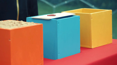 Three colourful wooden boxes: one which appears to be full of sand, one with a task brief laid on top of it, and the third which appears to be empty.