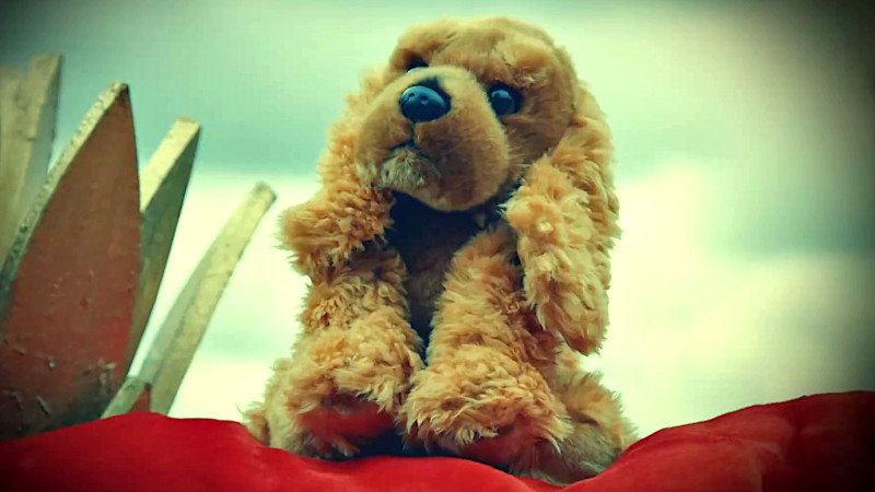 A stuffed toy dog on a pillow. A large golden ornamental pineapple can be seen in the background.